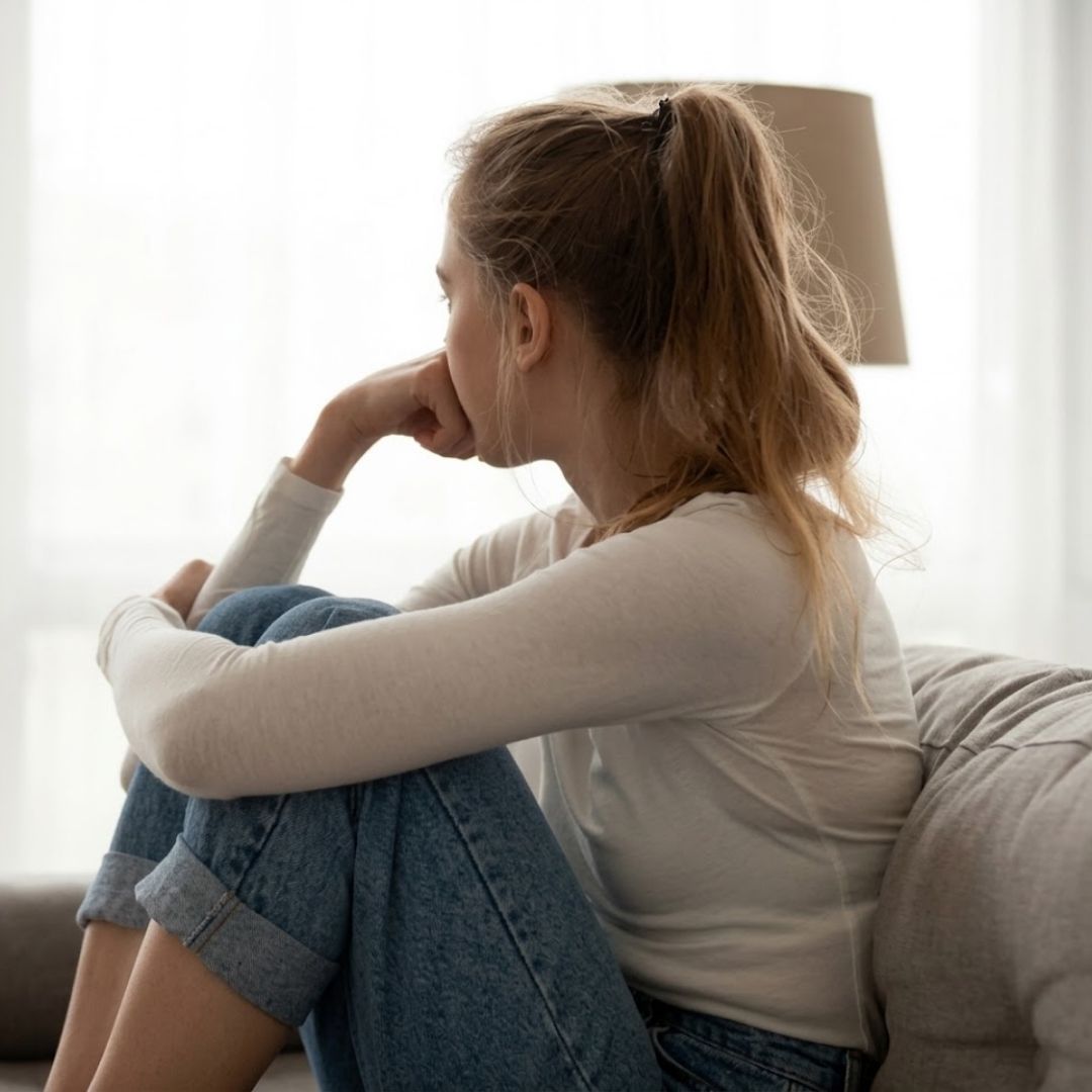 Adolescente pensive assise sur un canapé, regardant par la fenêtre